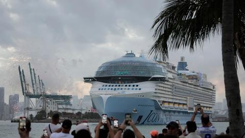 Menschen stehen in Miami am Ufer und fotografieren und filmen im Januar 2024 mit ihren Smartphones die Jungfernfahrt des weltgrößten Kreuzfahrtschiffes "Icon of the Seas",