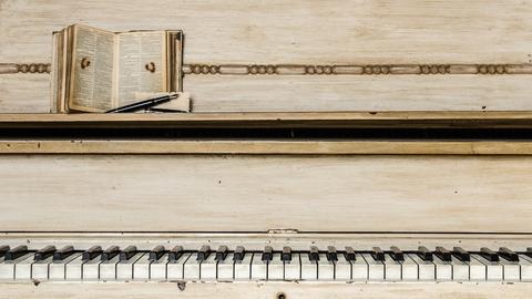 Musik hat eine besondere Anziehungskraft auf Schriftsteller und Autorinnen. Zu sehen ist ein Klavier mit heruntergespielten Tasten, auf der Ablage liegt eine Bibel oder ein ähnliches Buch mit klein geschriebenem Text. 