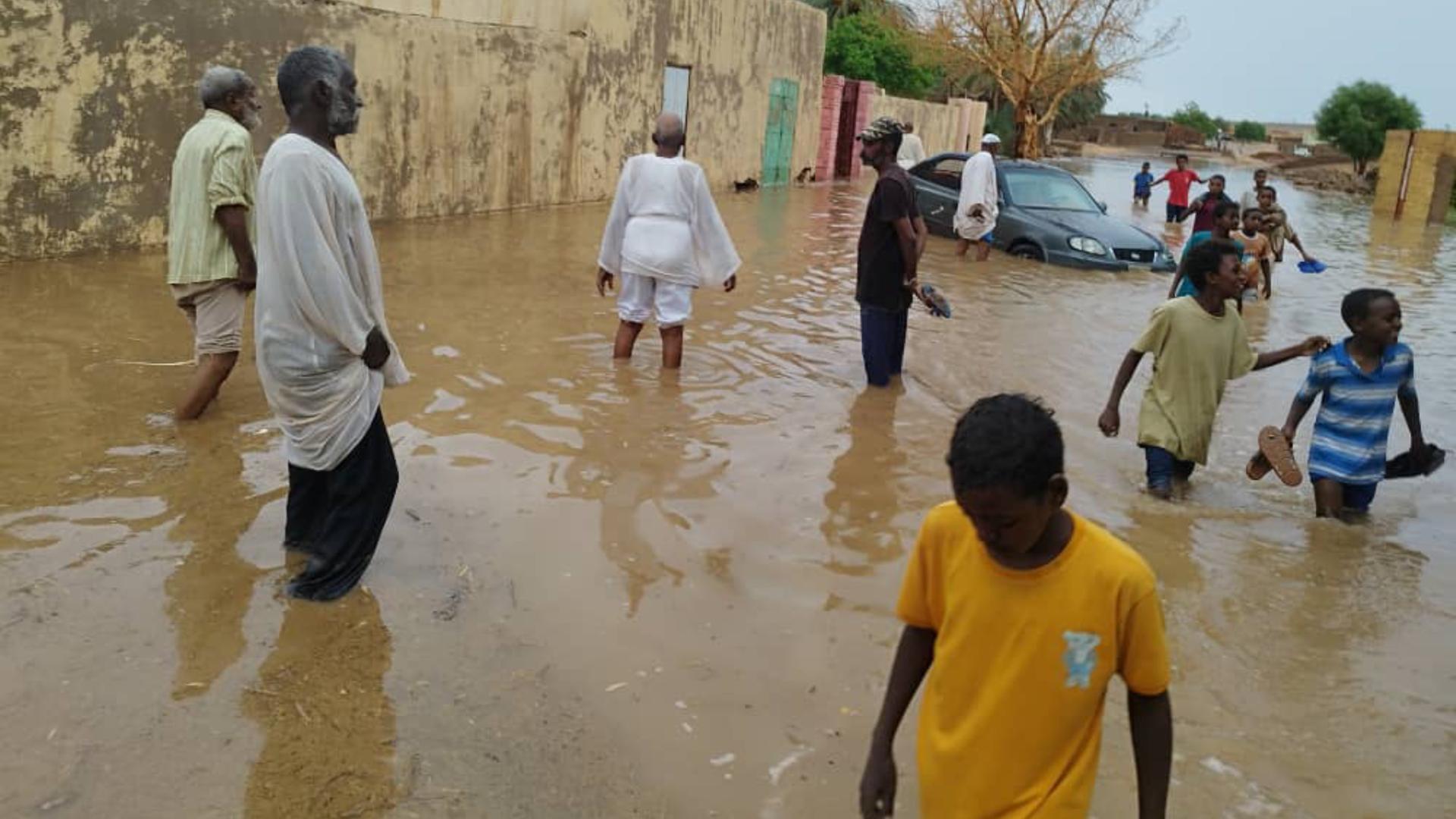 Sudan, Dongola: Menschen waten durch eine vom Hochwasser überschwemmte Straße im Sudan.