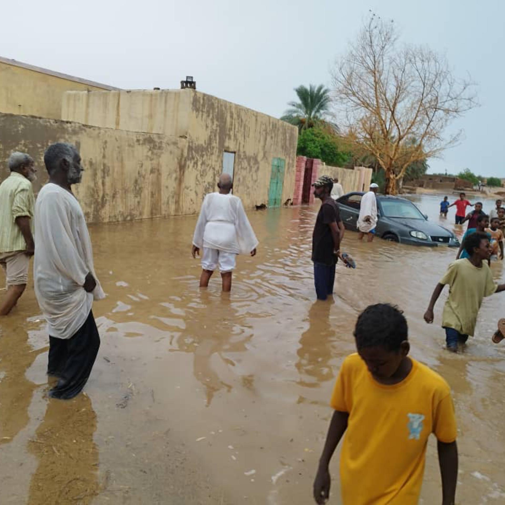 Sudan, Dongola: Menschen waten durch eine vom Hochwasser überschwemmte Straße im Sudan.