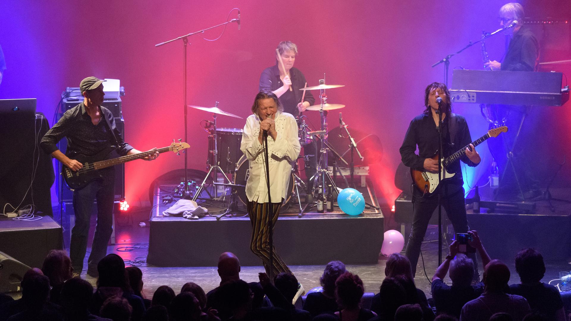 Die Band Fehlfarben mit Michael Kemner (Bass, ganz links), Peter Hein (Gesang), Saskia von Klitzing (Schlagzeug), Thomas Schneider (Gitarre) und Frank Fenstermacher (Keyboard) auf einer Bühne bei einem Konzert in Berlin in pink-violettem Licht