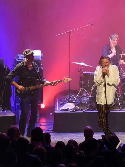Die Band Fehlfarben mit Michael Kemner (Bass, ganz links), Peter Hein (Gesang), Saskia von Klitzing (Schlagzeug), Thomas Schneider (Gitarre) und Frank Fenstermacher (Keyboard) auf einer Bühne bei einem Konzert in Berlin in pink-violettem Licht
