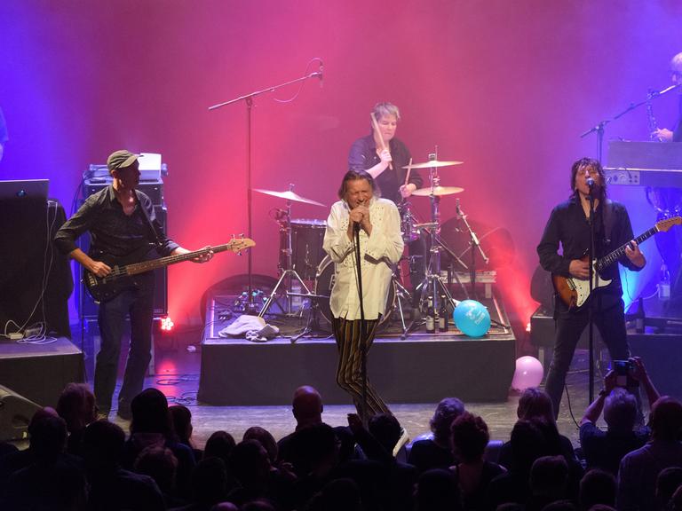 Die Band Fehlfarben mit Michael Kemner (Bass, ganz links), Peter Hein (Gesang), Saskia von Klitzing (Schlagzeug), Thomas Schneider (Gitarre) und Frank Fenstermacher (Keyboard) auf einer Bühne bei einem Konzert in Berlin in pink-violettem Licht