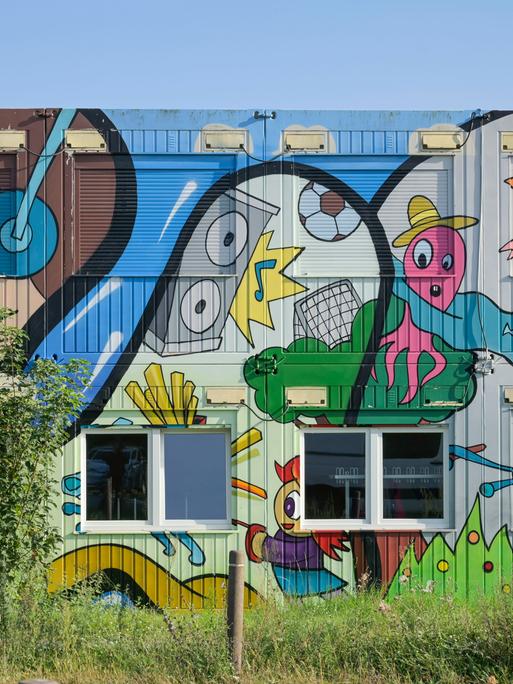 Ein mit bunten Comicmotiven - darunter ein Surfer, ein Teddy, ein Junge mit Kopfhörern und eine fußballspielenden Krake - bemalter Container einer Grund- und Oberschule in Schwanebeck in Brandenburg. Ein mit bunten Comicmotiven - darunter ein Surfer, ein Teddy, ein Junge mit Kopfhörern und eine fußballspielenden Krake - bemalter Container einer Grund- und Oberschule in Schwanebeck in Brandenburg.