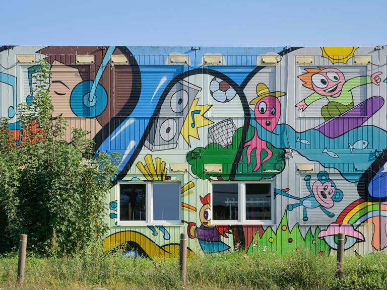 Ein mit bunten Comicmotiven - darunter ein Surfer, ein Teddy, ein Junge mit Kopfhörern und eine fußballspielenden Krake - bemalter Container einer Grund- und Oberschule in Schwanebeck in Brandenburg. Ein mit bunten Comicmotiven - darunter ein Surfer, ein Teddy, ein Junge mit Kopfhörern und eine fußballspielenden Krake - bemalter Container einer Grund- und Oberschule in Schwanebeck in Brandenburg.