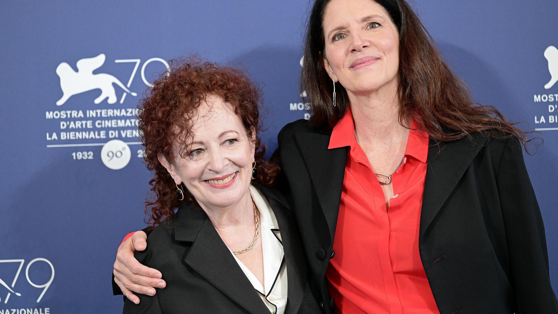 Laura Poitras und Nan Goldin stehen Arm in Arm vor einer Fotowand