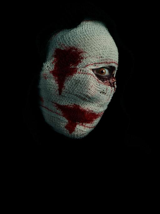 Halloween-Kostüm zeigt ein verbundenes Frauengesicht mit Blut um Mund und rechtes Auge.