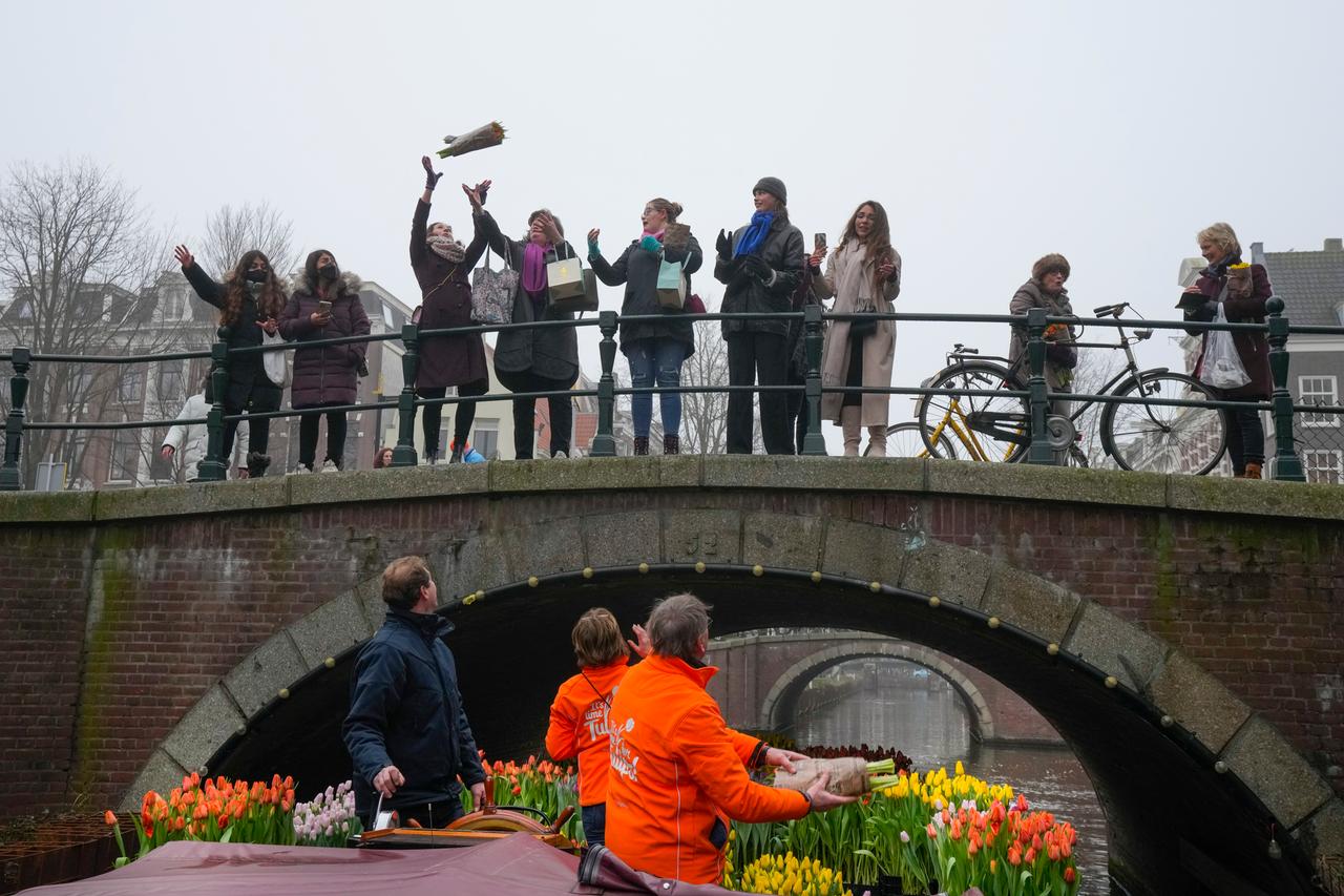 Ein Boot voller Tulpen fährt durch eine Gracht, Menschen auf einer Brücke fangen hochgeworfene Blumensträuße.