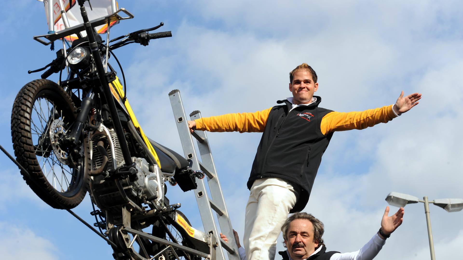 Der Hochseil-Artist Johann Traber (oben) und sein Vater Johann Traber Senior posieren am Donnerstag (24.09.2009) auf einem Hochseil an den Landungsbrücken in Hamburg neben einem Motorrad. Dreieinhalb Jahre nach seinem schweren Unfallist der Hochseil-Artist Johann Traber wieder in Hamburg aufgetreten. Mit seinem Motorrad fuhr der 25-Jährige auf dem Hochseil von der Brücke 4 an den Landungsbrücken bis zum alten Elbtunnel. Foto: Marcus Brandt dpa/lno (zu dpa/lno 0757 vom 24.09.2009) +++(c) dpa - Report+++