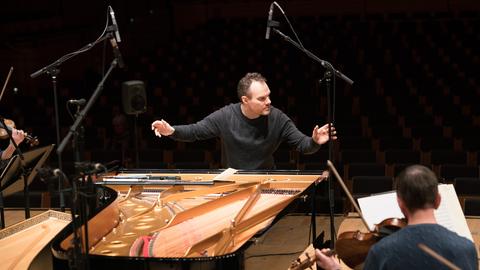 Der Pianist Lars Vogt sitzt am Flügel und hat die Arme fürs Dirigieren ausgebreitet, während er Blickkontakt zu den Musikern sucht.