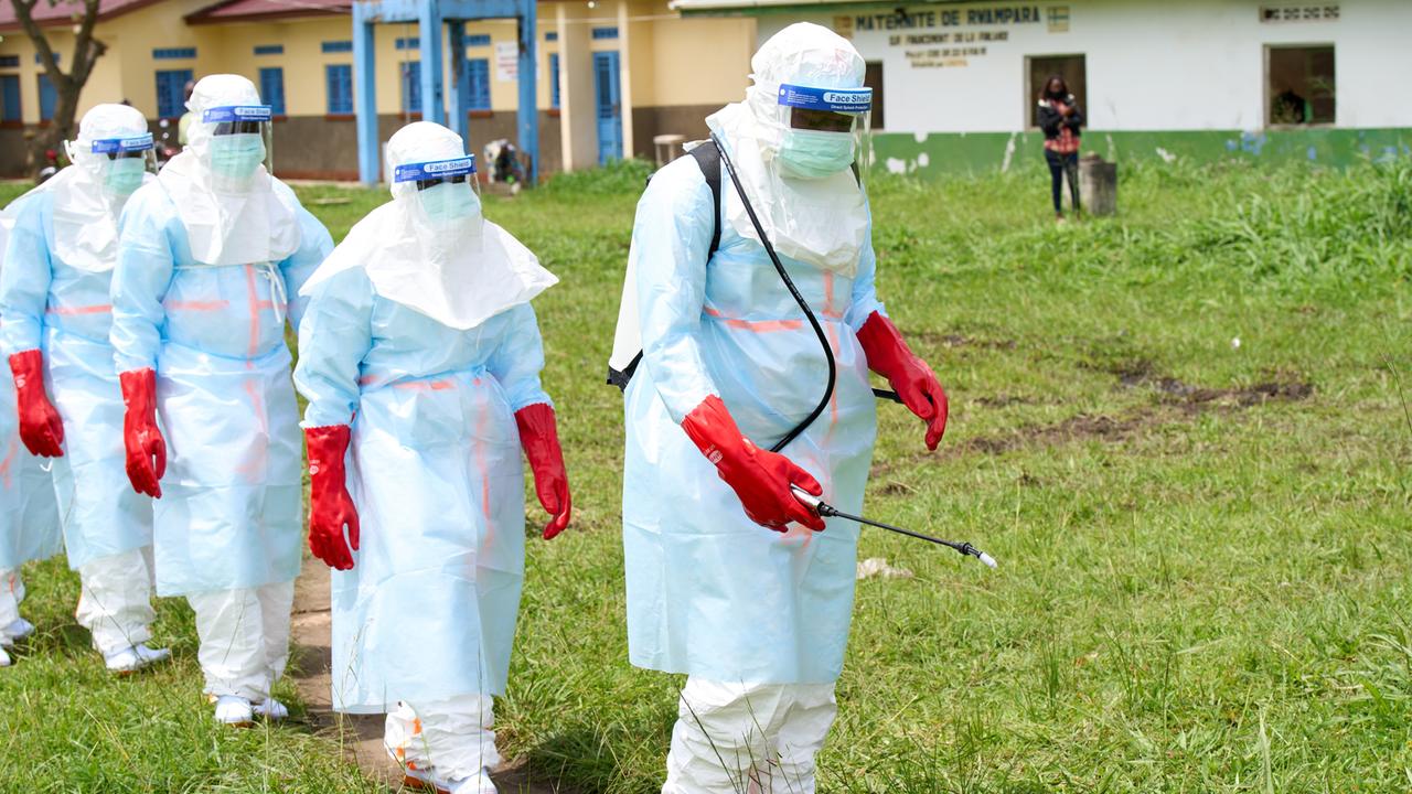 Mitarbeitende im Bezirk Rwampara im Kongo mit Desinfektionsmitteln. Sie sind komplett in weiße Overalls gehüllt, die sie vor dem Virus schützen sollen. In der Hand hält einer eine Spritze, wie man sie von Pflanzenschutzmitteln kennt. Mitarbeitende im Bezirk Rwampara im Kongo mit Desinfektionsmitteln. Sie sind komplett in weiße Overalls gehüllt, die sie vor dem Virus schützen sollen. In der Hand hält einer eine Spritze, wie man sie von Pflanzenschutzmitteln kennt.
