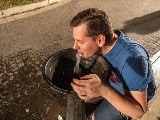 Ein Mann trinkt frisches Wasser aus einem öffentlichen Trinkbrunnen.