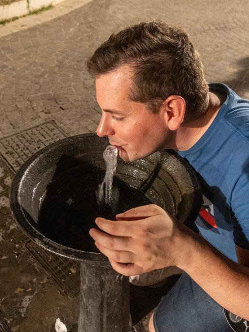 Ein Mann trinkt frisches Wasser aus einem öffentlichen Trinkbrunnen.