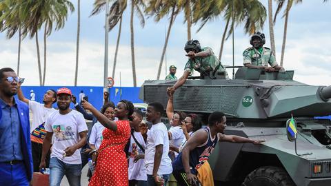 Menschen auf der Straße posieren mit Soldaten, die sich aus einem Panzer zu ihnen herunter beugen.