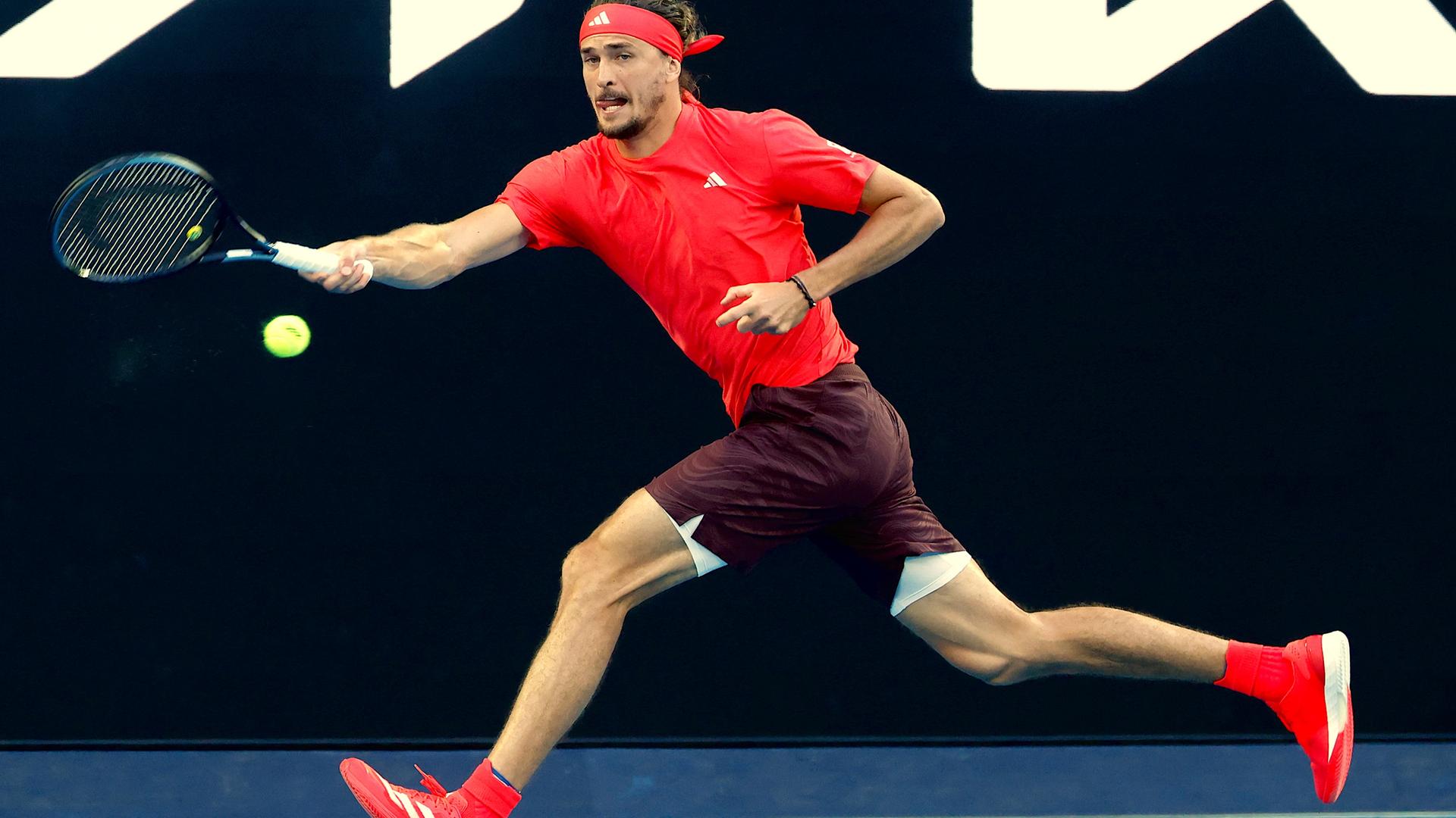 Zverev im roten Shirt und mit rotem Stirnband spielt im vollem Lauf eine Vorhand.