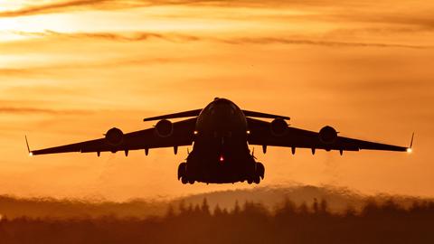Start einer C-17 Globemaster III von der US-Luftwaffenbasis Ramstein. Ein großes graues Flugzeug fliegt im Sonnenuntergang. 