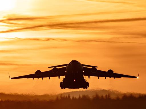 Start einer C-17 Globemaster III von der US-Luftwaffenbasis Ramstein. Ein großes graues Flugzeug fliegt im Sonnenuntergang. Start einer C-17 Globemaster III von der US-Luftwaffenbasis Ramstein. Ein großes graues Flugzeug fliegt im Sonnenuntergang.