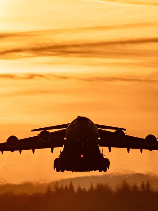 Start einer C-17 Globemaster III von der US-Luftwaffenbasis Ramstein. Ein großes graues Flugzeug fliegt im Sonnenuntergang. Start einer C-17 Globemaster III von der US-Luftwaffenbasis Ramstein. Ein großes graues Flugzeug fliegt im Sonnenuntergang.