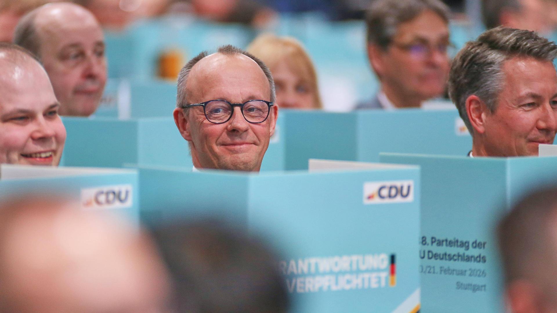 Bundeskanzler Friedrich Merz und andere CDU-Parteimitglieder sitzen hinter türkisfarbenen Tisch-Wahlkabinen.