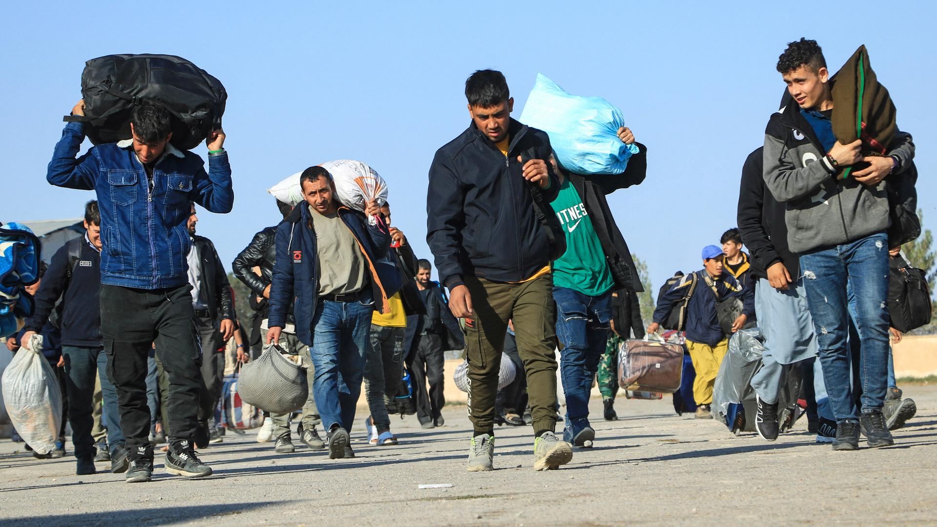 Männer gehen auf einer Straße in Afghanistan. Sie kommen aus dem Iran und tragen Säcke mit ihren Habseligkeiten auf ihren Schultern.