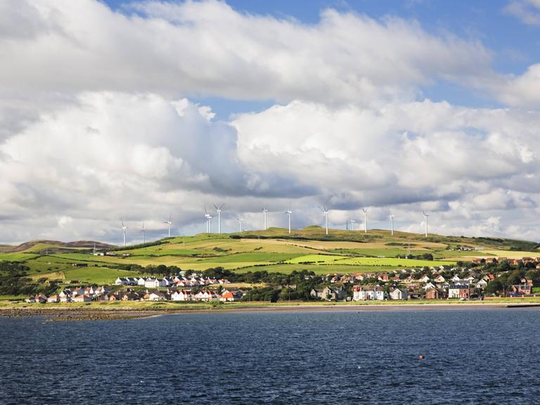 Windkrafträder nahe Ardrossan, North Ayyrshire, Schottland, Großbritannien. Das Bild ist vom Wasser aus aufgenommen, so dass im Vordergrund Meer zu sehen ist. Im Hintergrund sind Wolken am Himmel zu sehen.