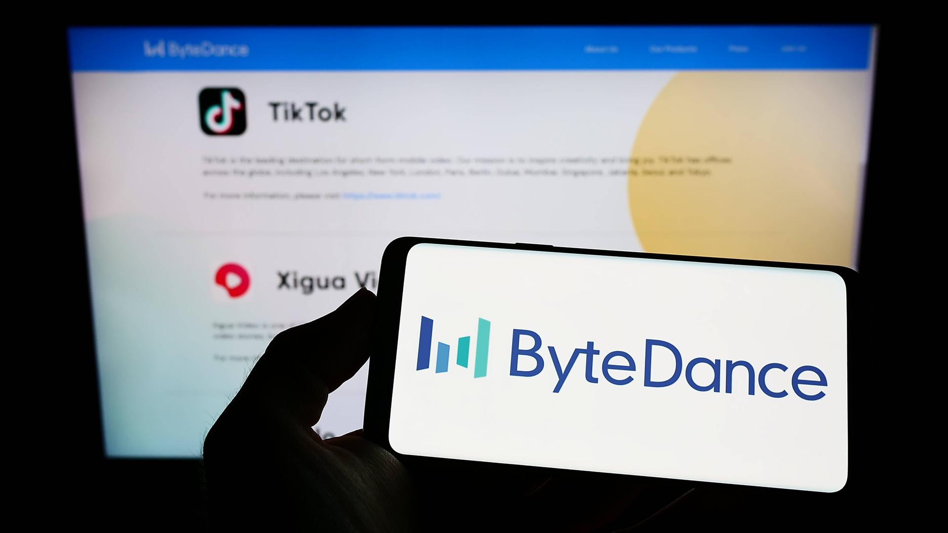 Auf einem Handydisplay ist der Schriftzug Bytedance zu sehen und dahinter ein TikTok-Logo auf einem Computerbildschrim.