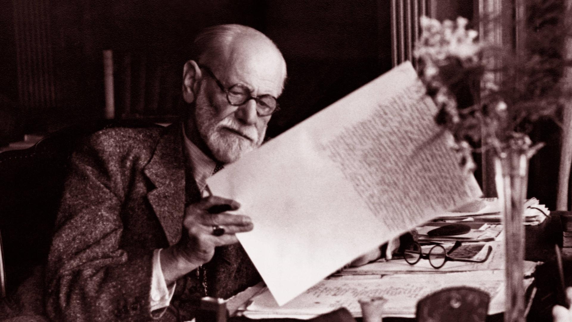 Sigmund Freud sitzt am Schreibtisch und liest ein Dokument