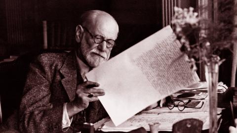Sigmund Freud sitzt am Schreibtisch und liest ein Dokument
