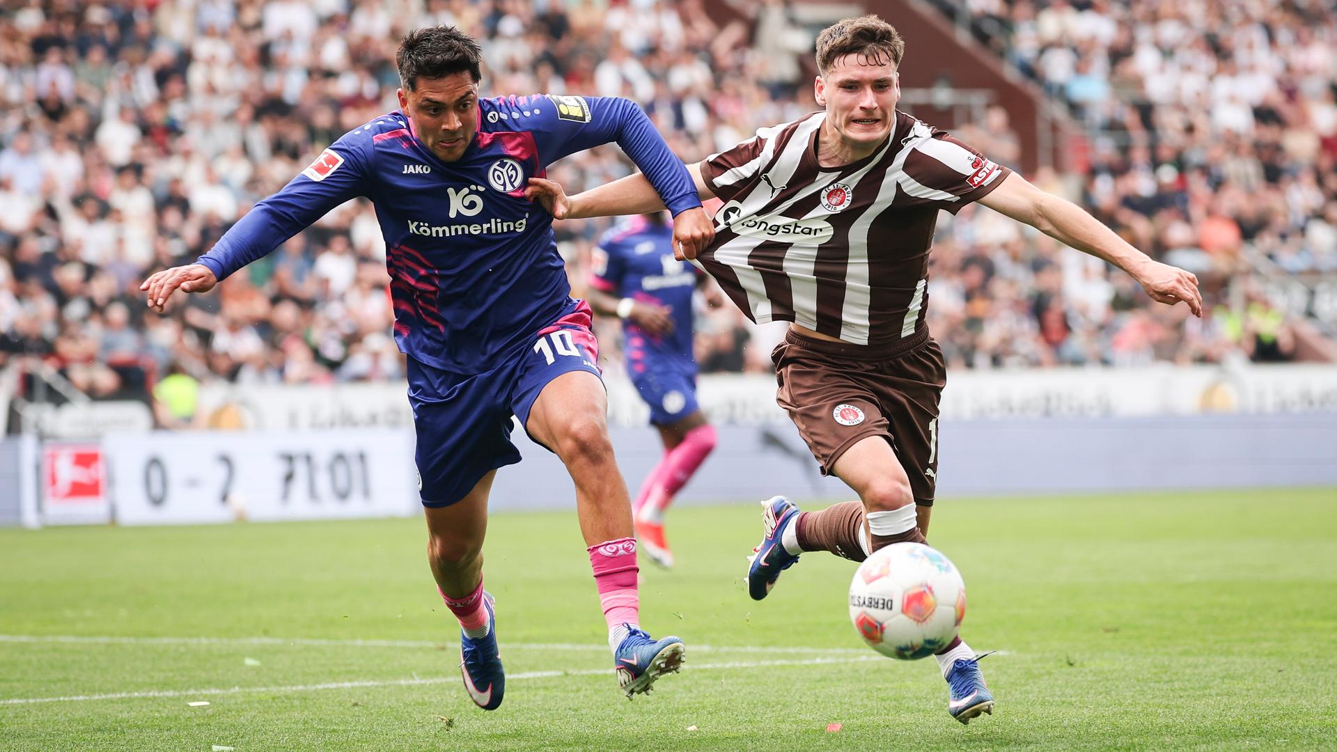 Die Spieler Nadiem Amiri (1. FSV Mainz 05) und Arkadiusz Pyrka (FC St. Pauli) zerren gegenseitig am Trikot und laufen dem Ball hinterher.