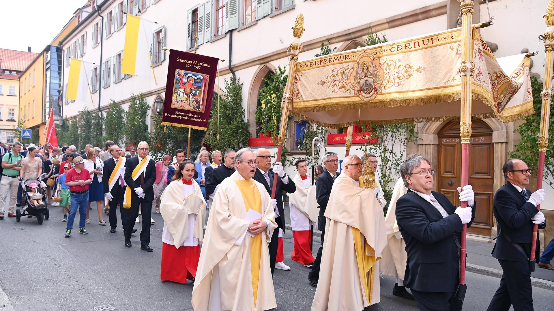 Das Foto zeigt eine Fronleichnamprozession. Zu sehen sind mehrere Geistliche sowie eine Monstranz unter einem Baldachin.