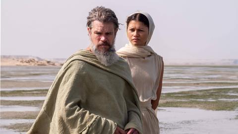 Matt Damon als Odysseus und Zendaya als Athena stehen vor einer Wüsten-ähnlichen Landschaft. Matt Damon als Odysseus und Zendaya als Athena stehen vor einer Wüsten-ähnlichen Landschaft.