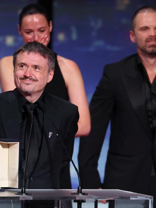 Cristian Mungiu steht an einem Rednerpult und lächelt. Vor ihm steht die Goldene Palme in einer Schatulle. 