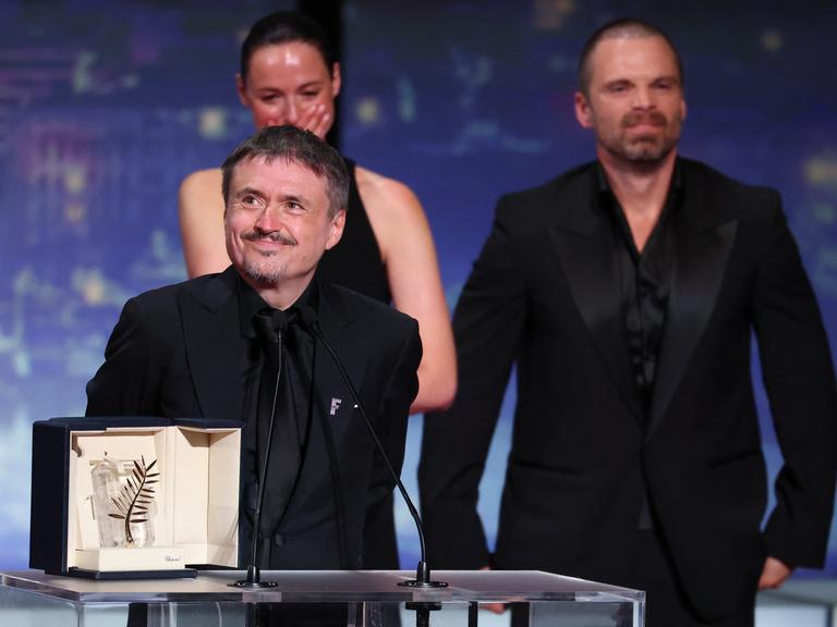 Cristian Mungiu steht an einem Rednerpult und lächelt. Vor ihm steht die Goldene Palme in einer Schatulle. 
