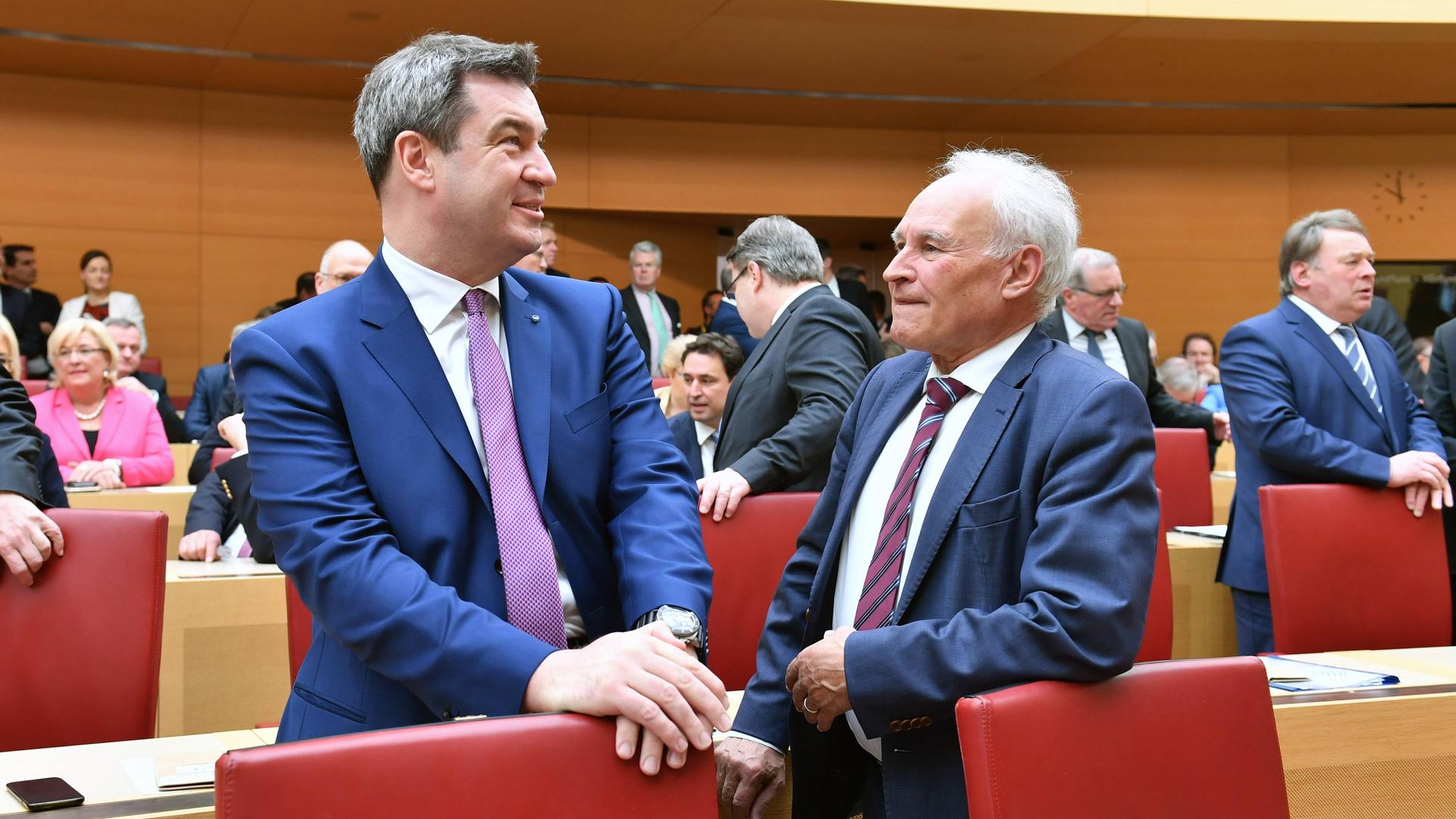Bayerns Ministerpräsident Markus Söder steht neben dem ehemaligen CSU-Vorsitzenden Erwin Huber in einem Parlamentsaal. Söder legt die Hände auf einen Stuhl und blickt in die Ferne, Huber an ihm vorbei.