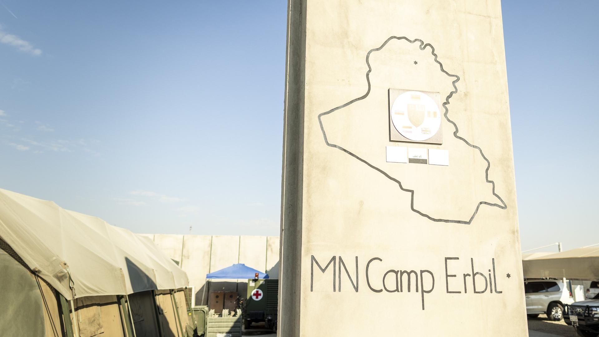 Ein Schild mit der Aufschrift "MN Camp Erbil" steht vor grünen Militärzelten.