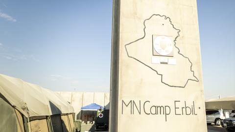 Ds helle Schild mit der Aufschrift "MN Camp Erbil" steht vor grünen Militärzelten.