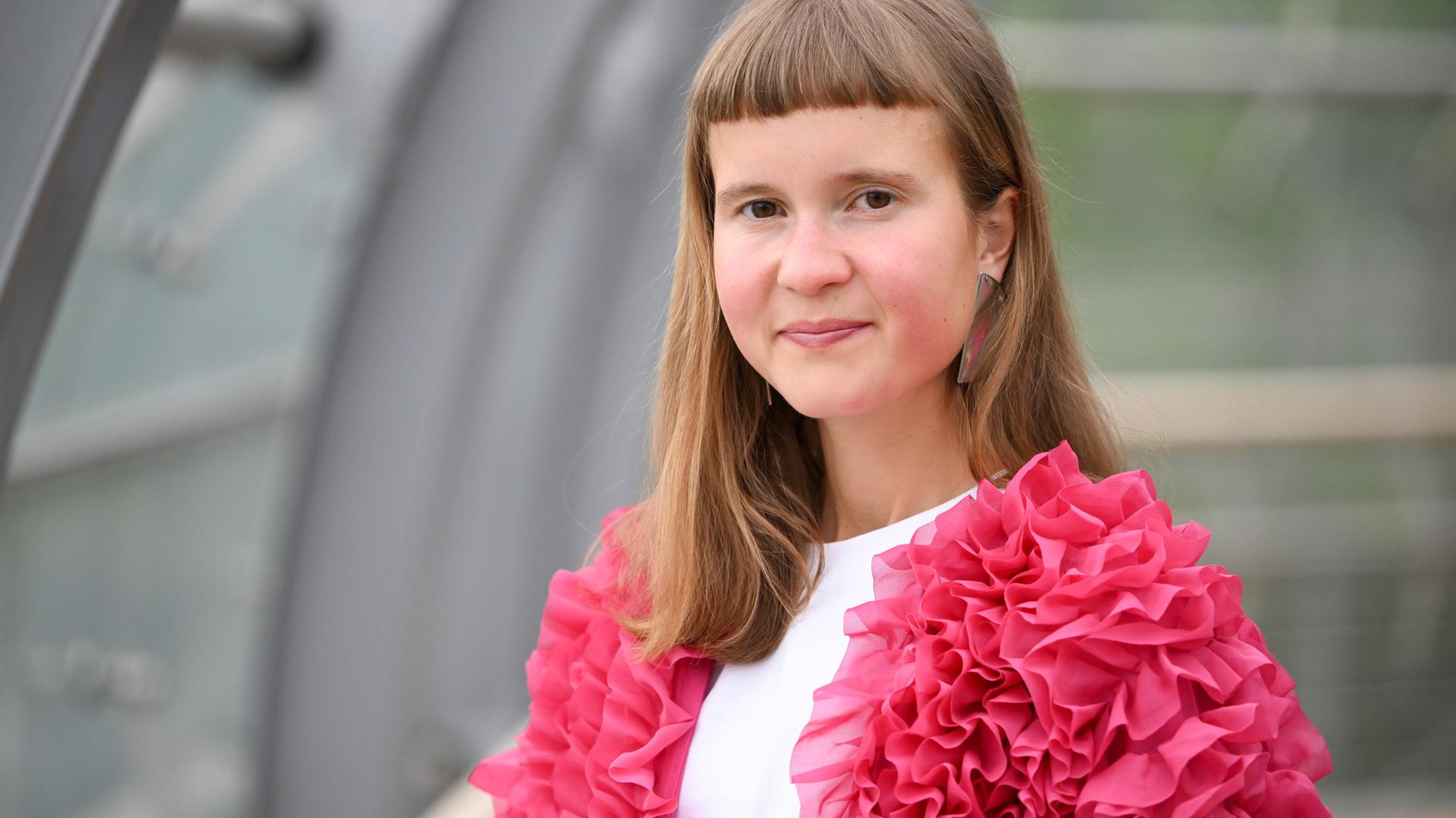 Eine junge Frau mit ungewöhnlicher Pnyfrisur und einer pinken Jacke schaut in die Kamera: die Schriftstellerin Caroline Wahl Eine junge Frau mit ungewöhnlicher Pnyfrisur und einer pinken Jacke schaut in die Kamera: die Schriftstellerin Caroline Wahl