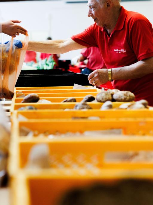 Ein Mitarbeiter der Berliner Tafel steckt ein Brot in die Tasche einer Frau.