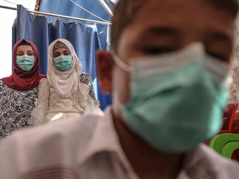 Das Foto zeigt drei syrische Kinder und Jugendliche in einem Waisenhaus in Idlib mit Gesichtsmasken. 