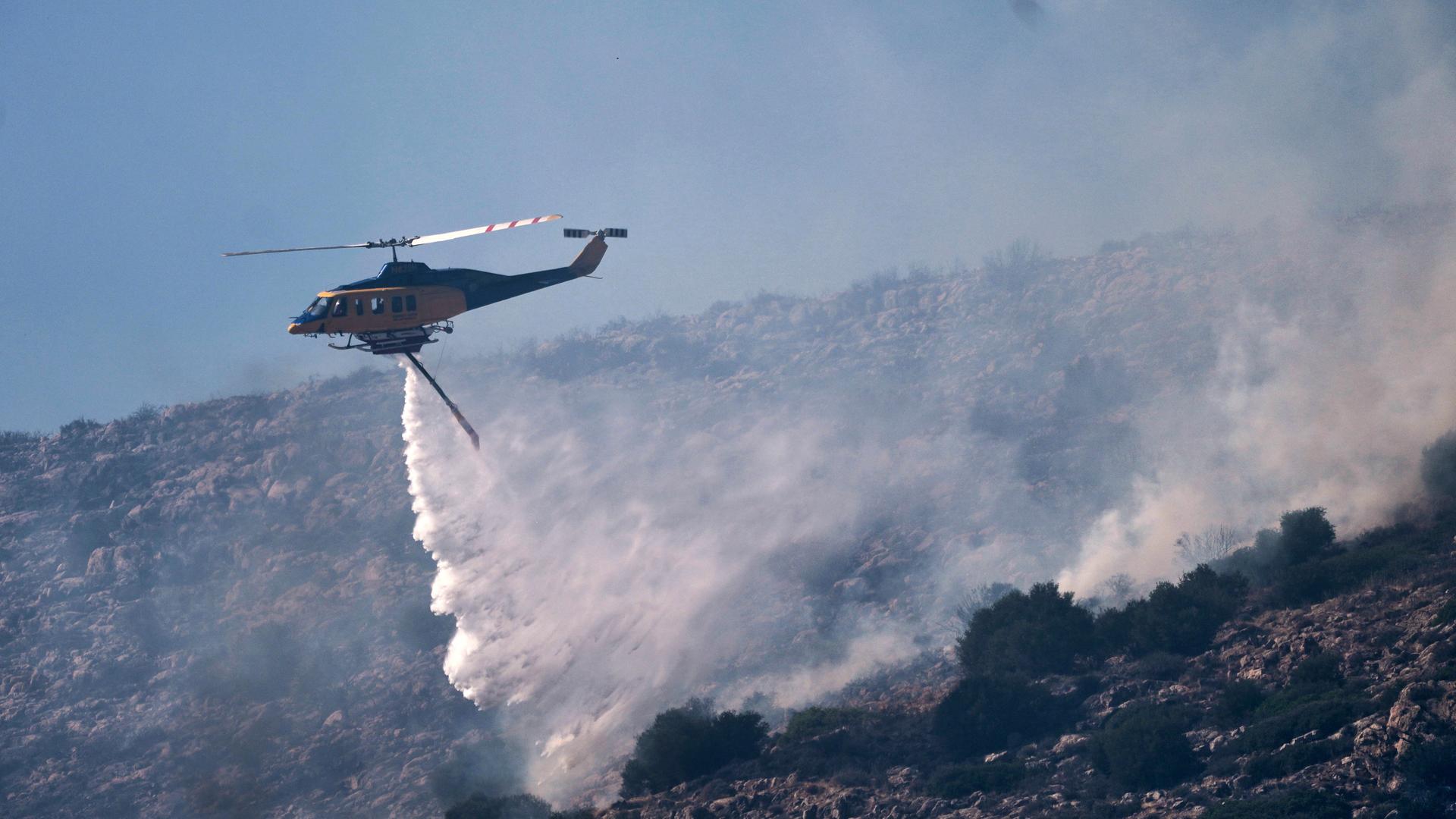 Ein Feuerwehrhubschrauber wirft Wasser über einem Feuer in der Küstengegend von Palaia Fokaia, südlich von Athen, ab. 
