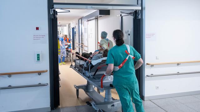 Eine Kranken-Pflegerin schiebt eine Liege mit einem Patienten in eine Not-Aufnahme. 