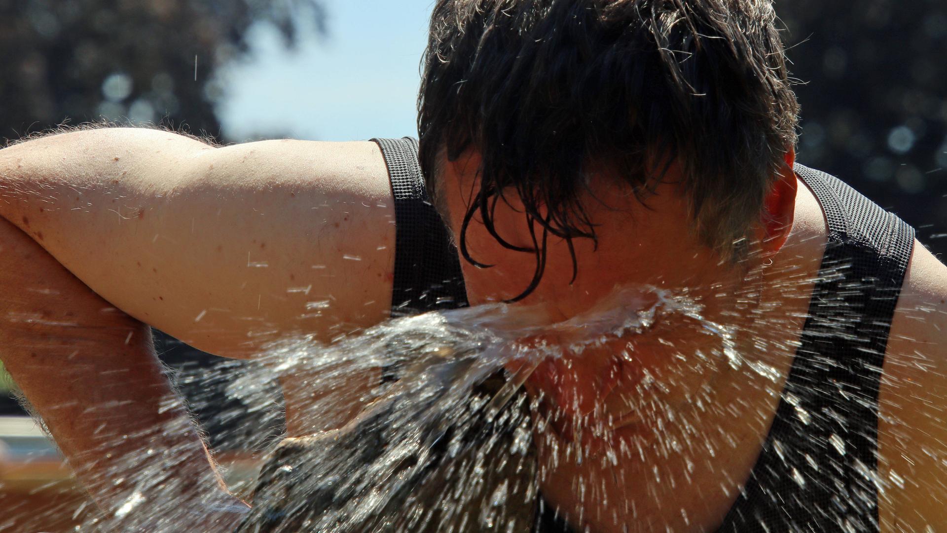 Ein Mann hält sein Gesicht in einen Wasserstrahl. Er beugt sich dafür runter. Sein Gesicht ist ganz rot. Ein Mann hält sein Gesicht in einen Wasserstrahl. Er beugt sich dafür runter. Sein Gesicht ist ganz rot.
