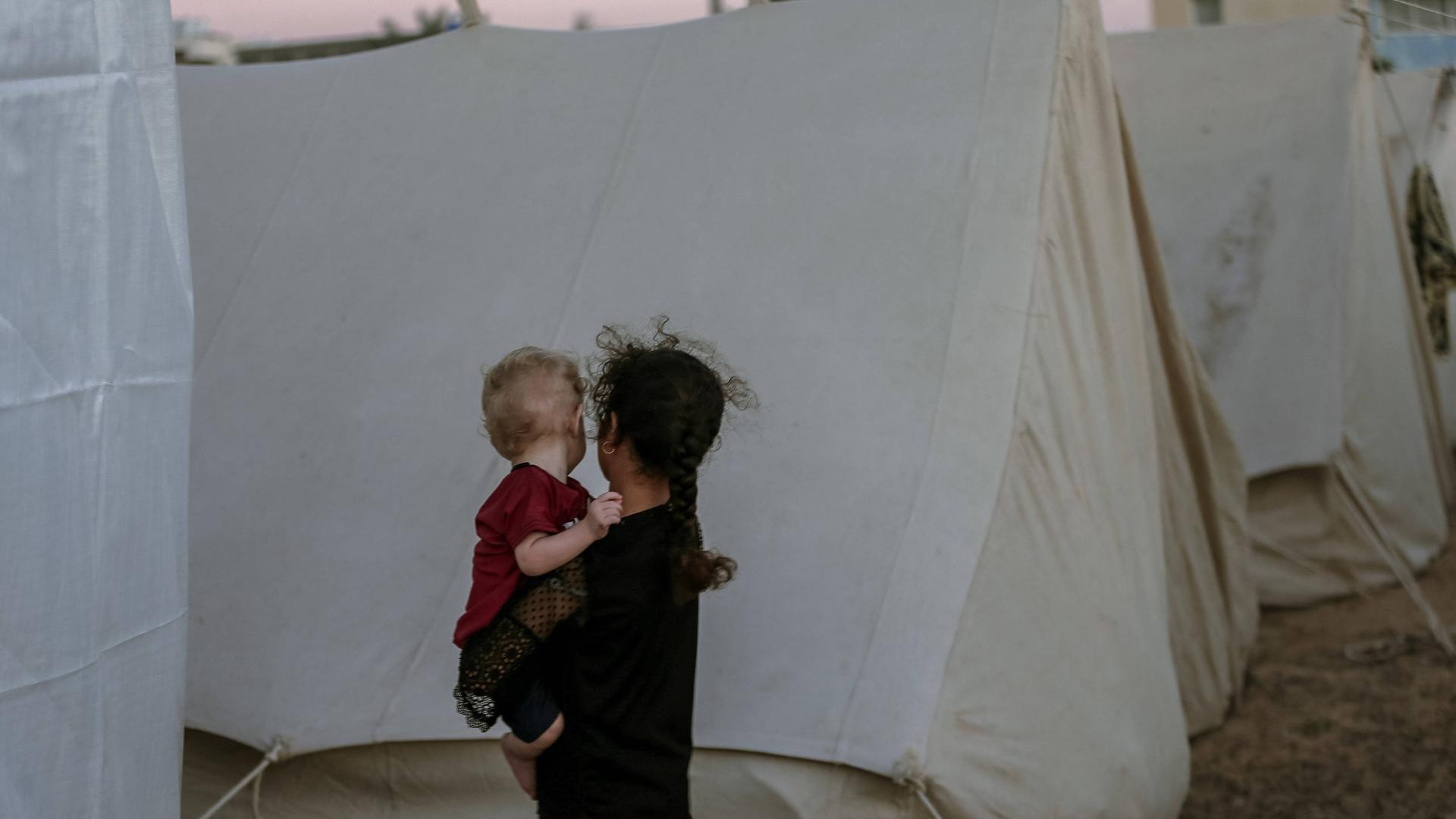 Ein junges palästinensisches Mädchen hält ein Baby, während es zwischen Zelten in einem Flüchtlingslager im südlichen Gazastreifen umhergeht. 