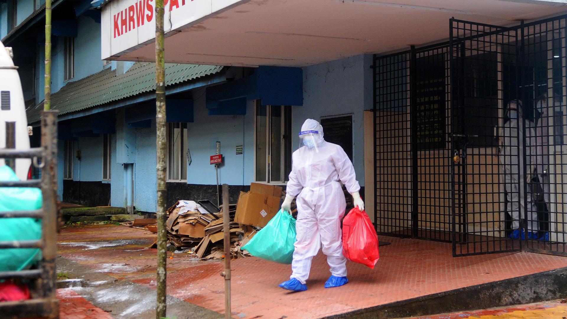 Eine Person im Seuchenschutzanzug trägt Müllsäcke aus dem Kozhikode Medical College Krankenhaus in Indien.