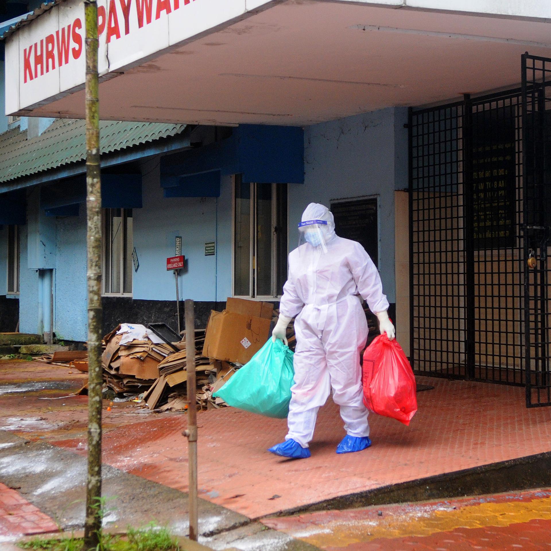 Eine Person im Seuchenschutzanzug trägt Müllsäcke aus dem Kozhikode Medical College Krankenhaus in Indien.