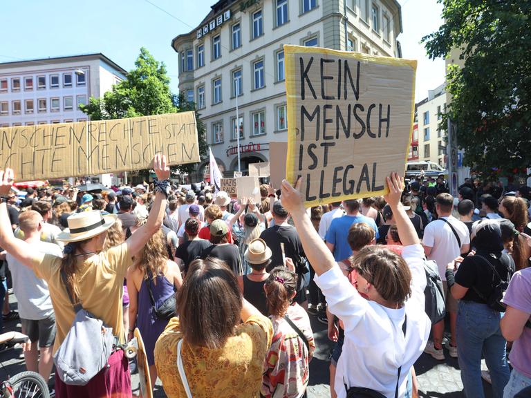 Menschen demonstrieren nahe einer Gedenkstele zum Gedenken an die Opfer einer Messerattacke von 2021 mit Plakaten auf denen "Menschenrechte statt rechte Menschen" und "Kein Mensch ist illegal" zu lesen ist, gegen eine Kundgebung der AfD.