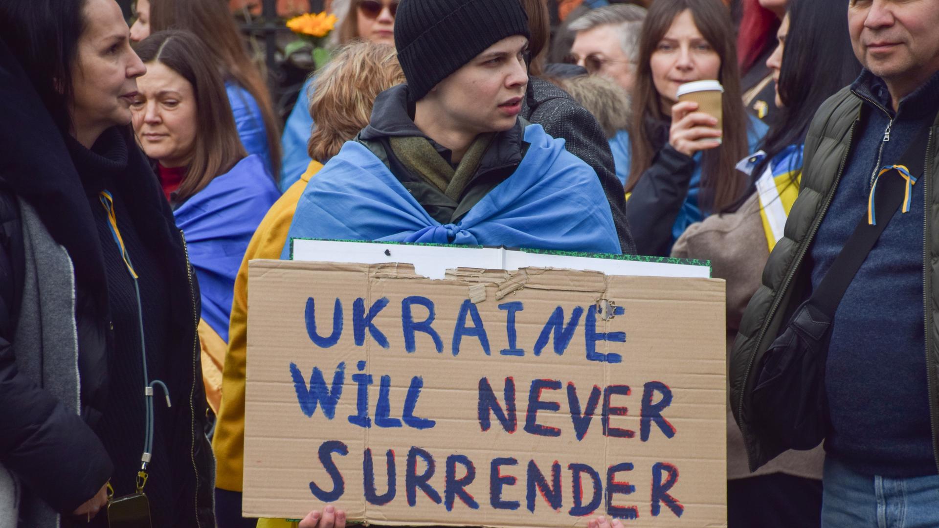 Ein Demonstrant auf einer Demo in Großbritannien hält ein Schild mit der Aufschrift: "Ukraine will never surrender."