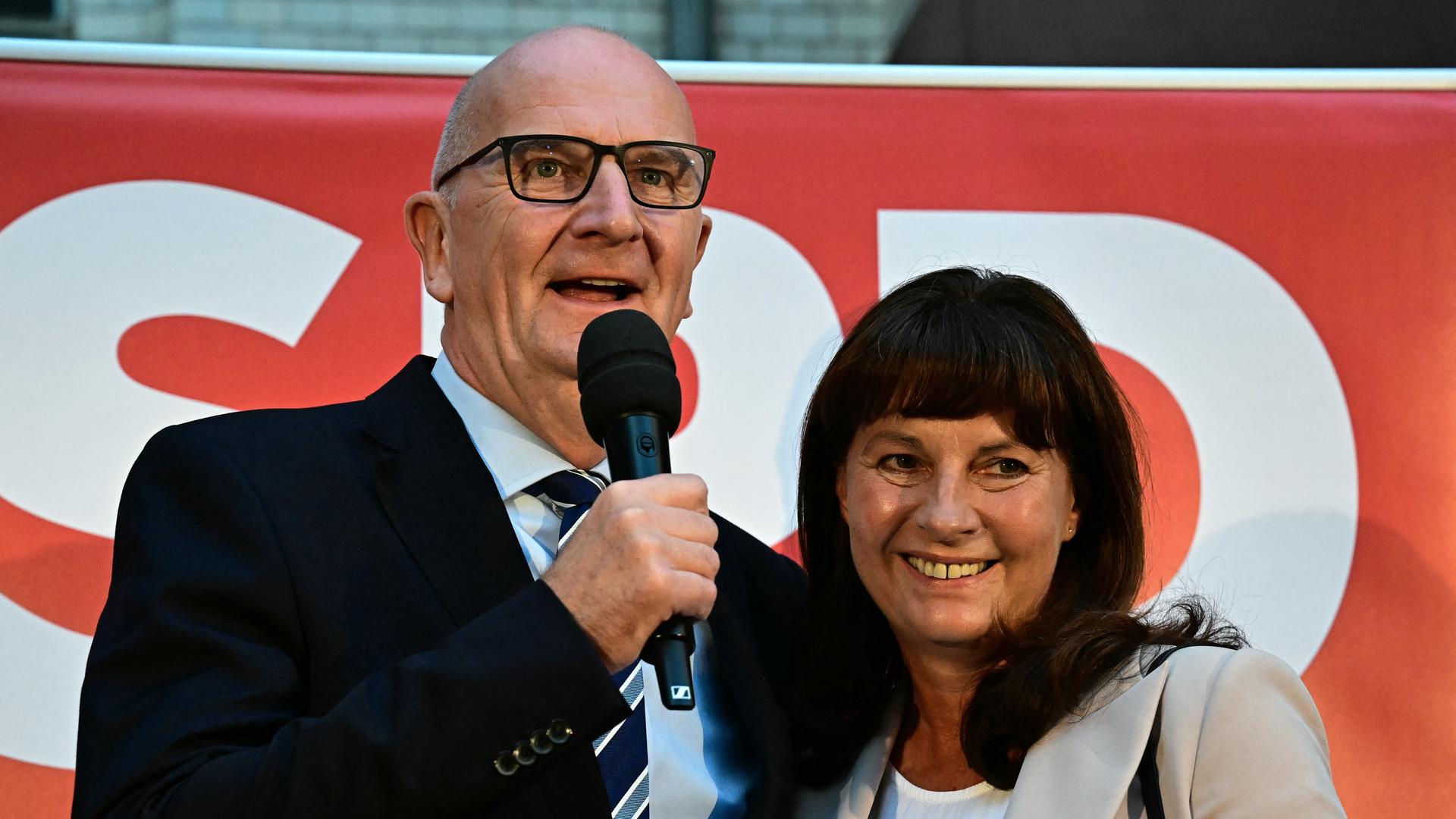 Ein Mann und eine Frau stehen auf einer Bühne. Dahinter steht ein SPD-Plakat.