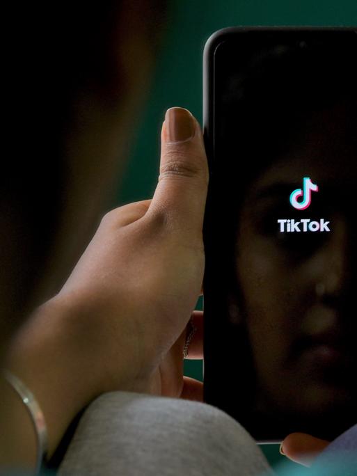 Nahaufnahme von Händen, die ein Smartphone mit geöffneter Tiktok-App halten.