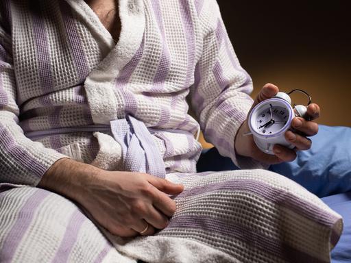 Stilisiertes Foto eines Mannes im Bademantel, der eine Uhr in der Hand hält